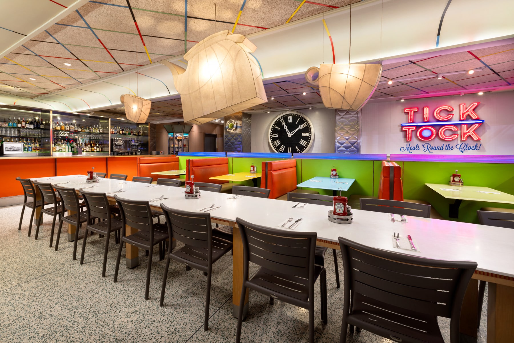 tick tock diner for breakfast with large long table with cutlery set, large light shades and a large clock, retro diner style