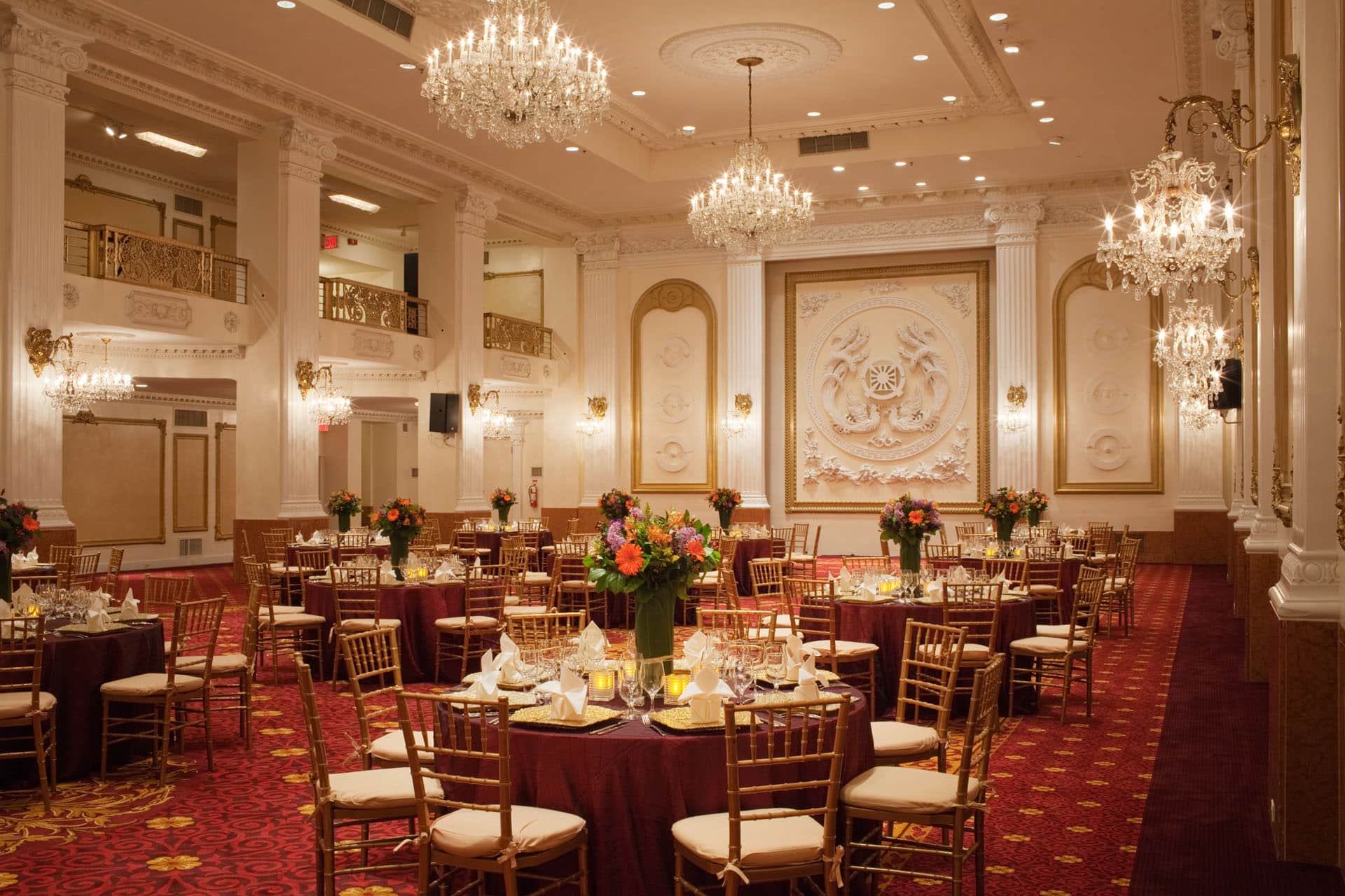 grand ballroom with chandeliers red carpet and multiple tables set for dining