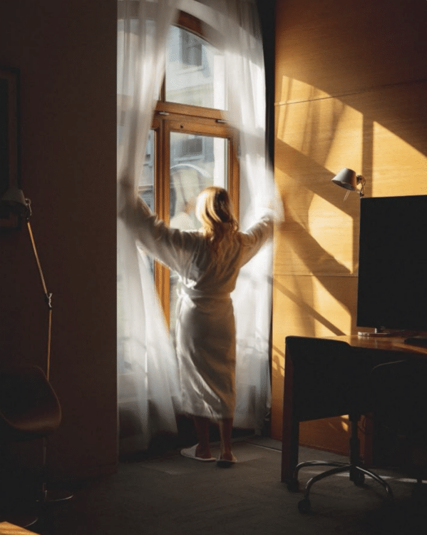 woman opening large windows in hotel with sun shining whilst wearing robe in nyc