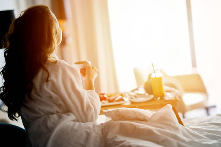 woman enjoying morning coffee overlooking new york at sunrise whilst sat on bed
