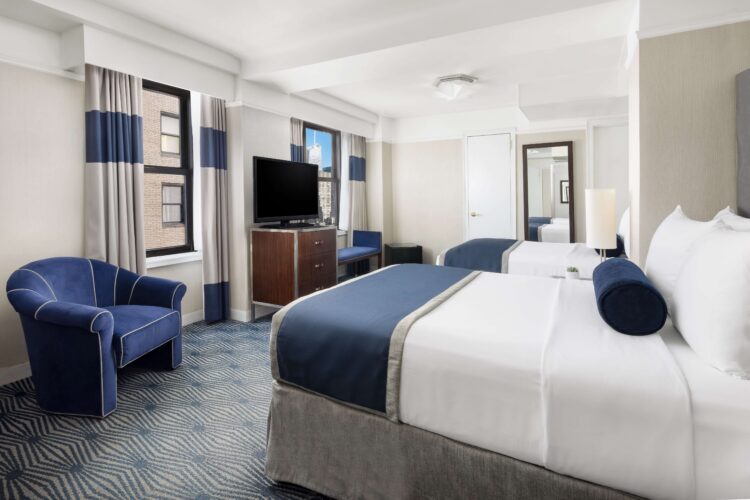 Executive double room with two beds, blue furnishings, TV stand, and city view window