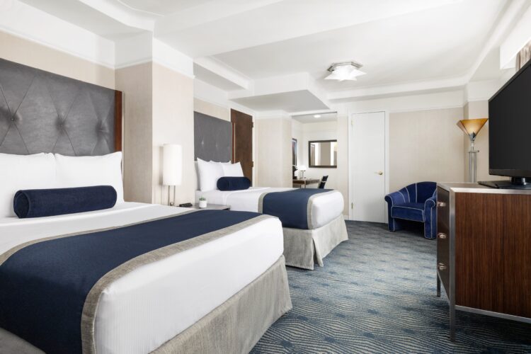 executive double suite room with two double beds facing a large television set with blue armchair