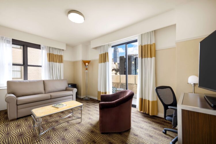 Accessible family suite living area with sofa, armchair, desk, and large windows with city views