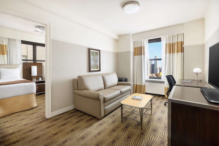 Family suite living room with sofa bed, coffee table, workspace, and city view through large window