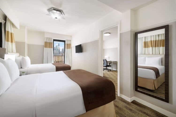 Accessible family suite with two queen beds, wall mirror, separate workspace, and city view window