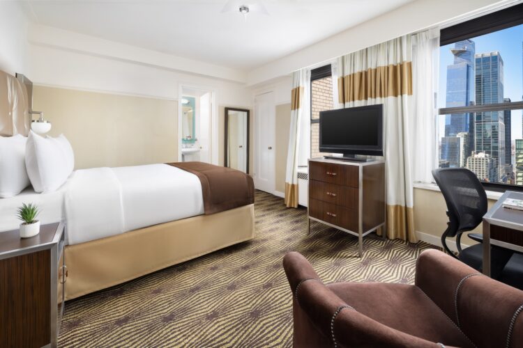 hotel queen suite at the new yorker with large window view of new york skyline, double bed with beige design