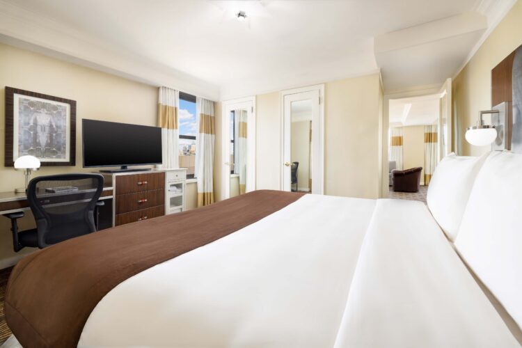 Queen terrace suite bedroom with king bed, dresser, TV, and city view window