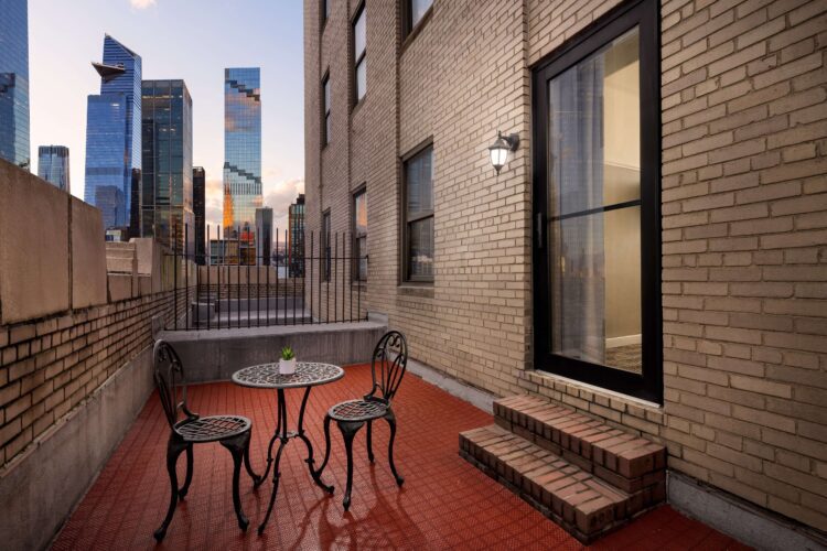 Private terrace with bistro table and chairs, brick walls, and city skyline views at sunset