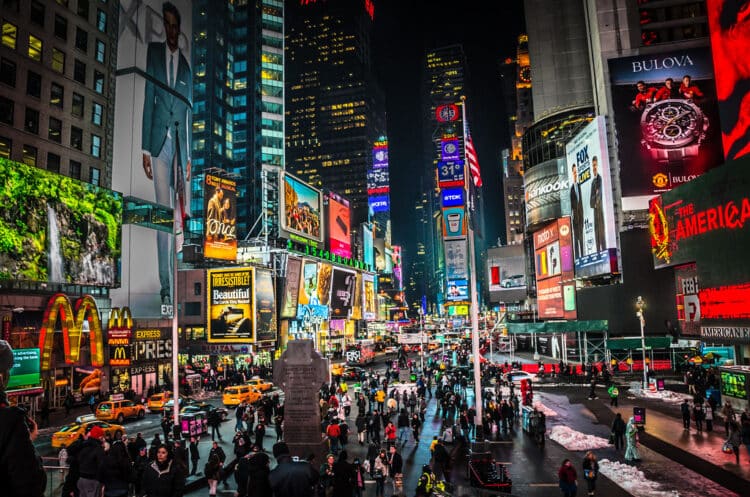 times square at night with bright lights, people walking through and view of billboards lighting sky